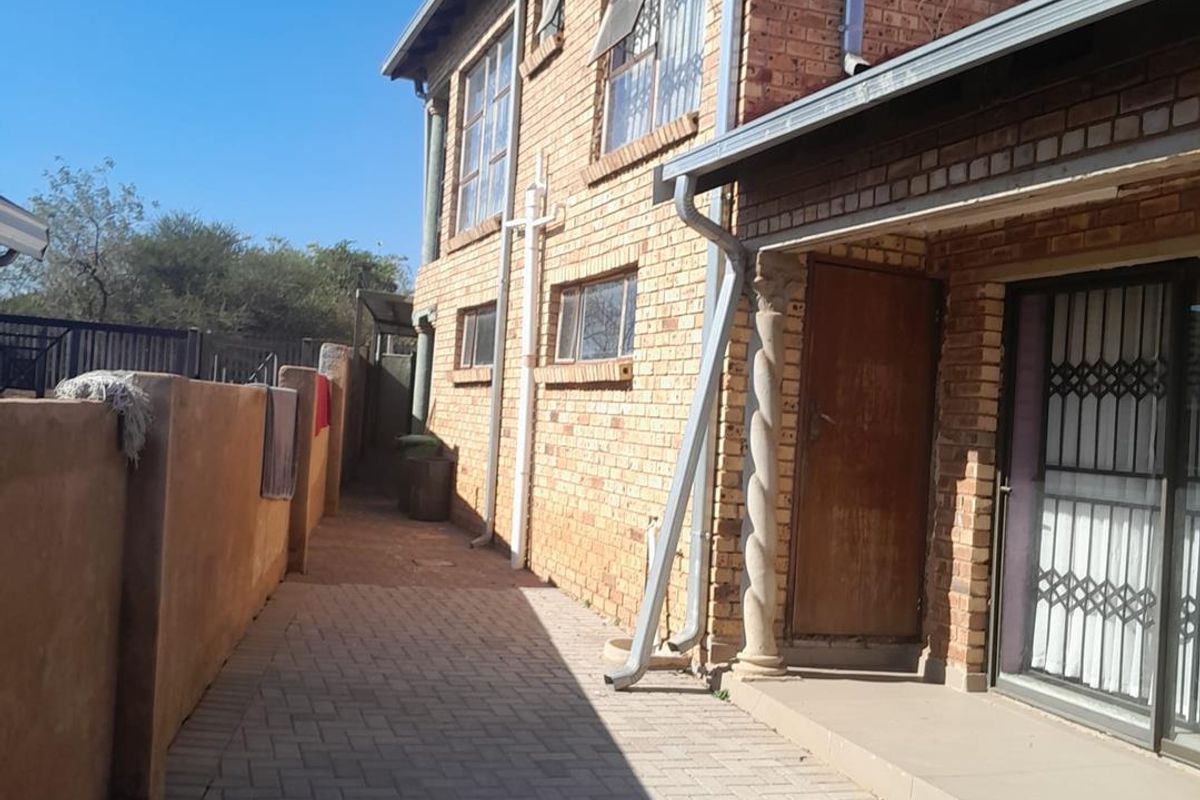 A side view of the property featuring a face brick facade, paved walkway, and a sliding door entrance with security gate.
