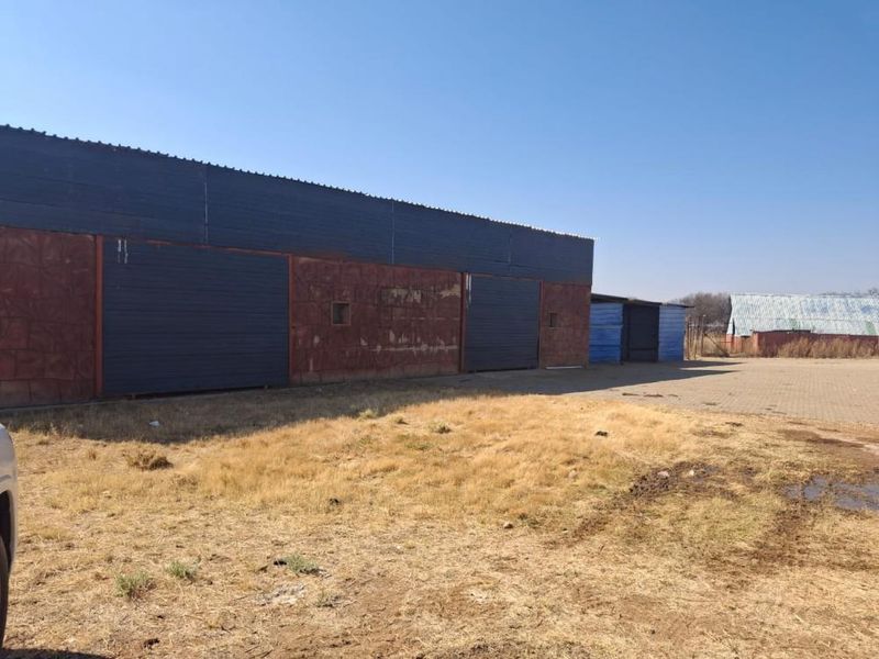 Exterior view of a large industrial-style outbuilding or warehouse on a small holding, featuring multiple sliding doors and a paved yard area.