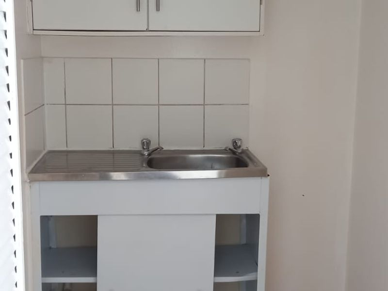 A compact scullery or utility area featuring a stainless steel sink, tiled splashback, and basic cabinetry in need of maintenance.