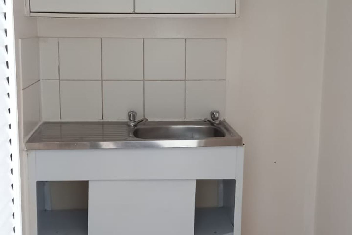 A compact scullery or utility area featuring a stainless steel sink, tiled splashback, and basic cabinetry in need of maintenance.