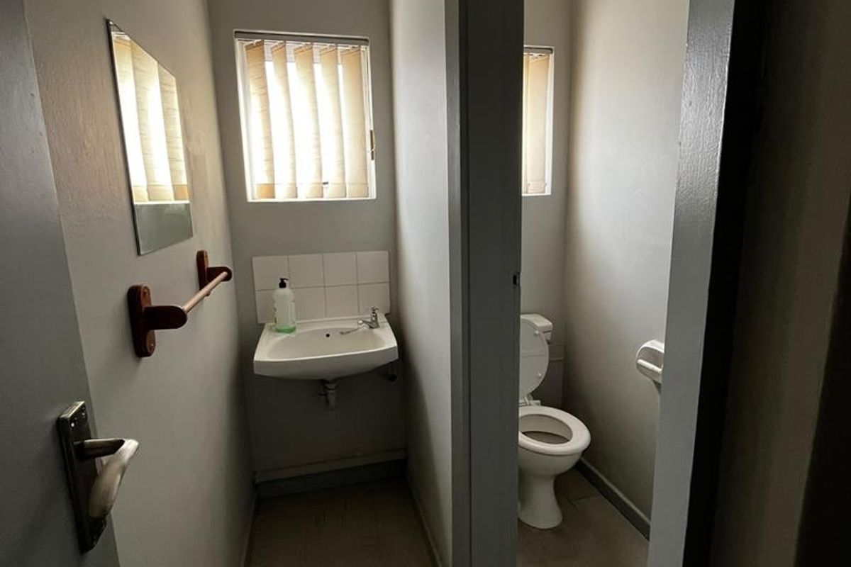 A functional office restroom featuring a wall-mounted basin and a separate toilet cubicle with neutral finishes.
