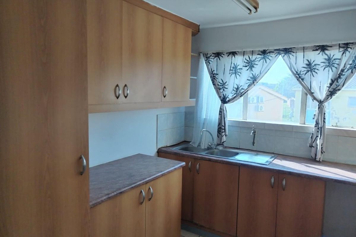 A functional kitchen featuring wood-look laminate cabinetry, laminate countertops, and a double bowl stainless steel sink with a tiled splashback.