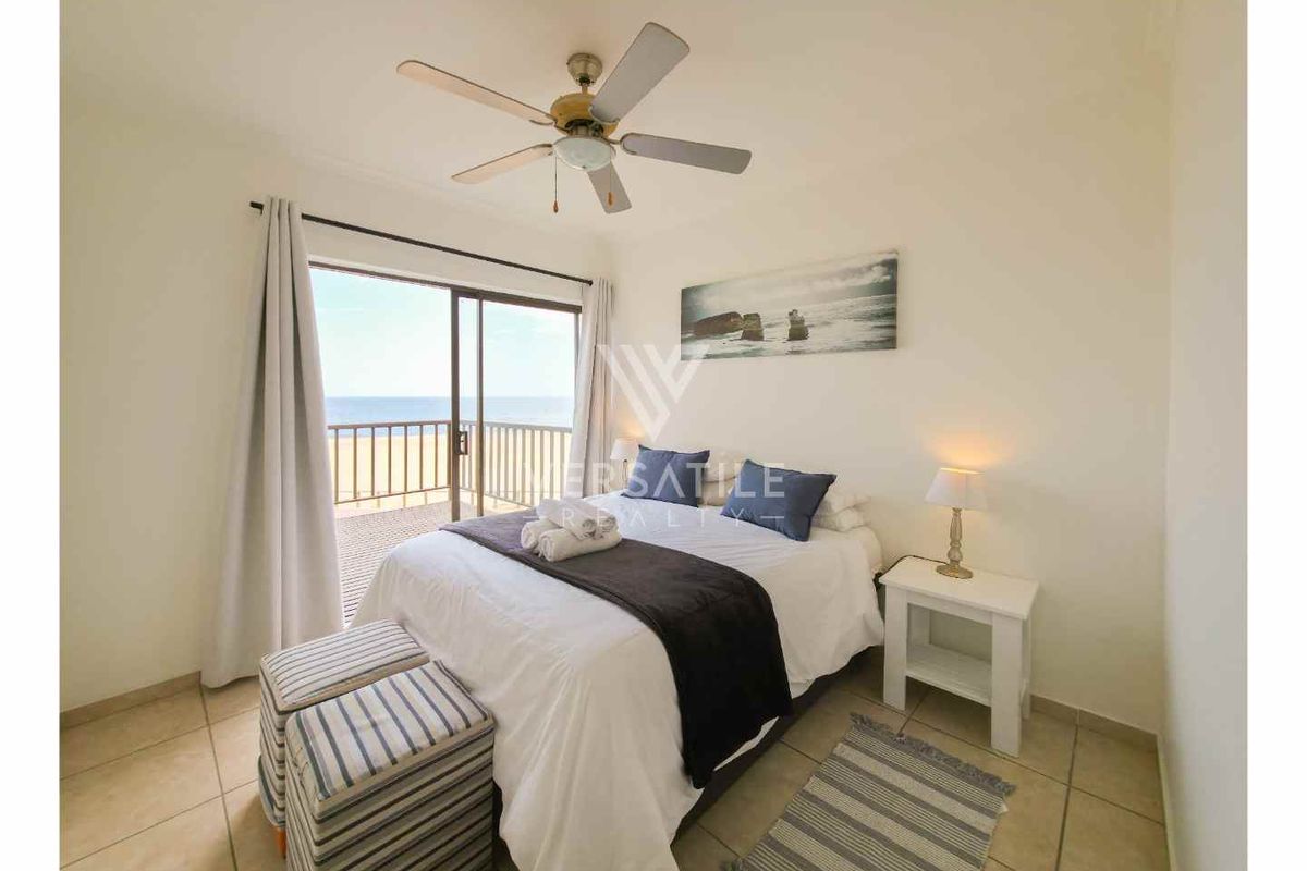 A bright bedroom featuring tiled flooring, a ceiling fan, and sliding glass doors that open onto a balcony with ocean views.
