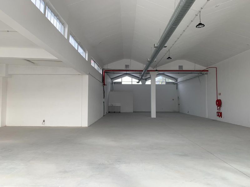Spacious open-plan retail unit featuring high ceilings, exposed industrial ducting, polished concrete floors, and abundant natural light from clerestory windows.