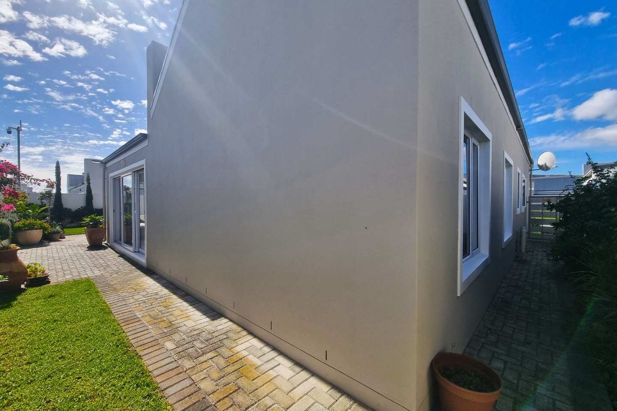 Side view of the property showing paved walkways, manicured lawn, and exterior wall finishes with sliding glass doors leading to the garden area.