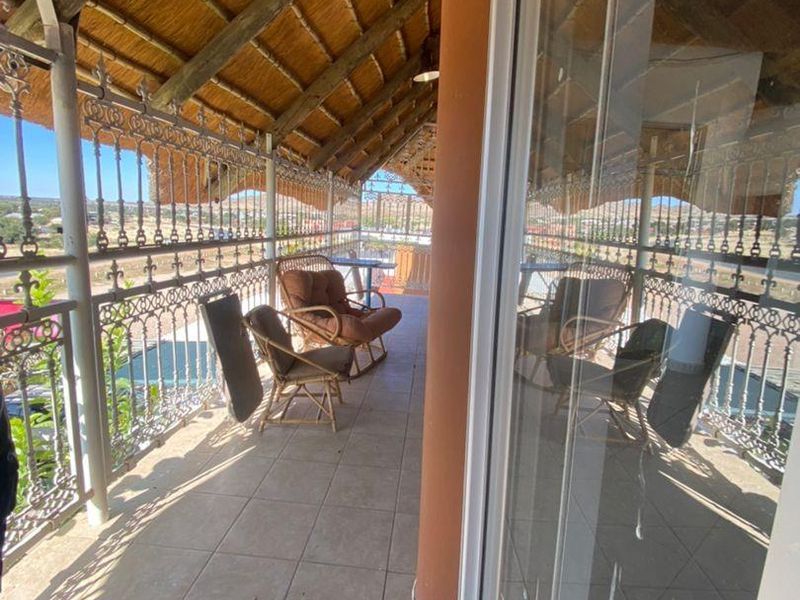 A covered balcony featuring a traditional thatched roof, tiled flooring, and decorative wrought iron railings, offering an open outdoor space.