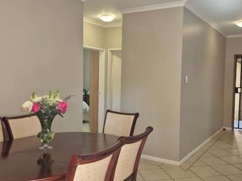 A neutral-toned living and dining area featuring tiled flooring, cove cornicing, and a secure entrance gate leading to the exterior.