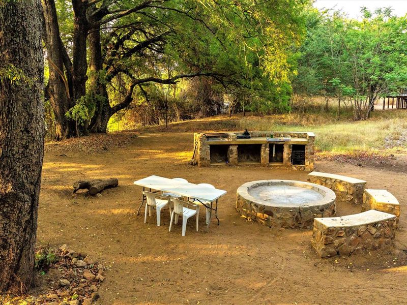 Outdoor entertainment area featuring a stone-built braai station and a circular stone fire pit with integrated bench seating in a natural bush setting.