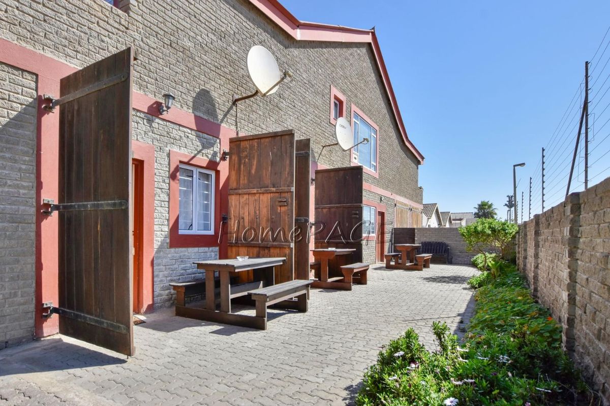 A paved rear patio area featuring multiple access points to the guest house units, enclosed by a perimeter wall with integrated security fencing.