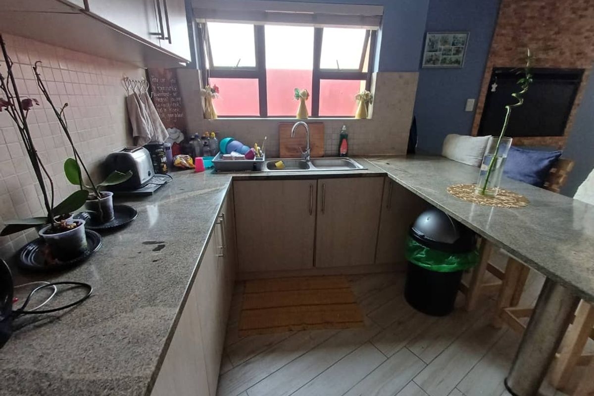 A functional kitchen featuring granite countertops, a double sink, light wood cabinetry, and a breakfast bar area with tiled flooring.