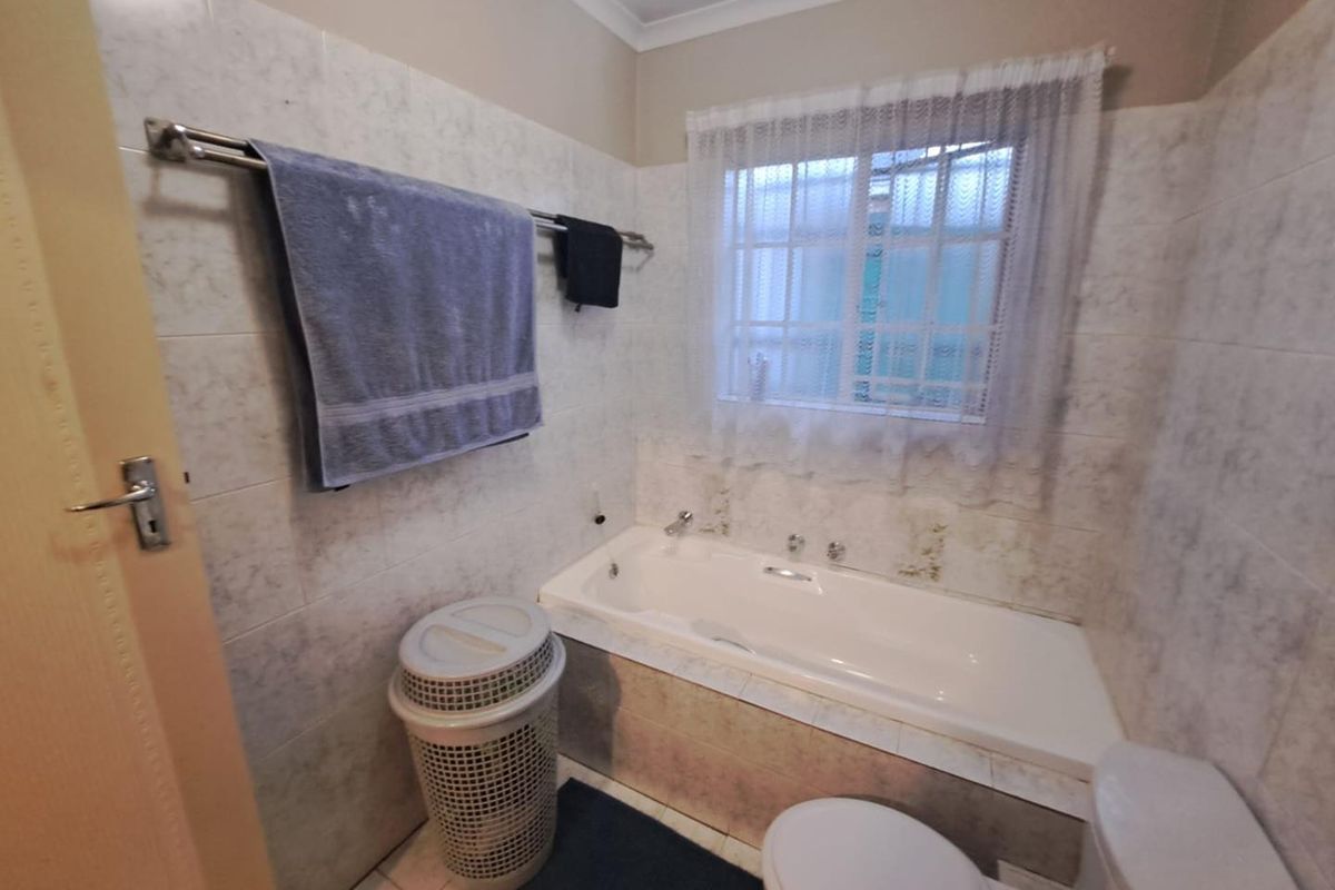 A functional bathroom featuring a built-in bathtub, tiled walls, and a window with security bars.