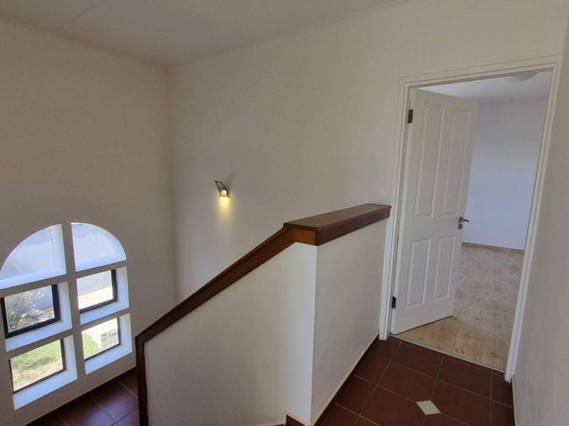 A bright landing area featuring an arched window, wooden handrail, and tiled flooring, leading into an adjacent room.