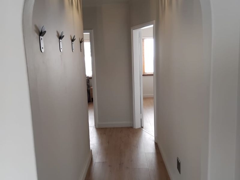 A bright and clean hallway featuring an elegant arched entrance, modern laminate flooring, and neutral wall finishes with convenient wall-mounted hooks.