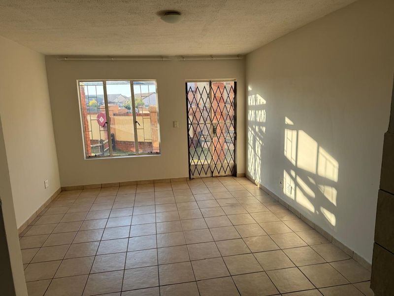 An empty living room featuring tiled flooring, a security gate, and a sliding door leading to the exterior.