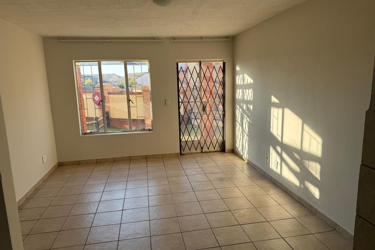An empty living room featuring tiled flooring, a security gate, and a sliding door leading to the exterior.