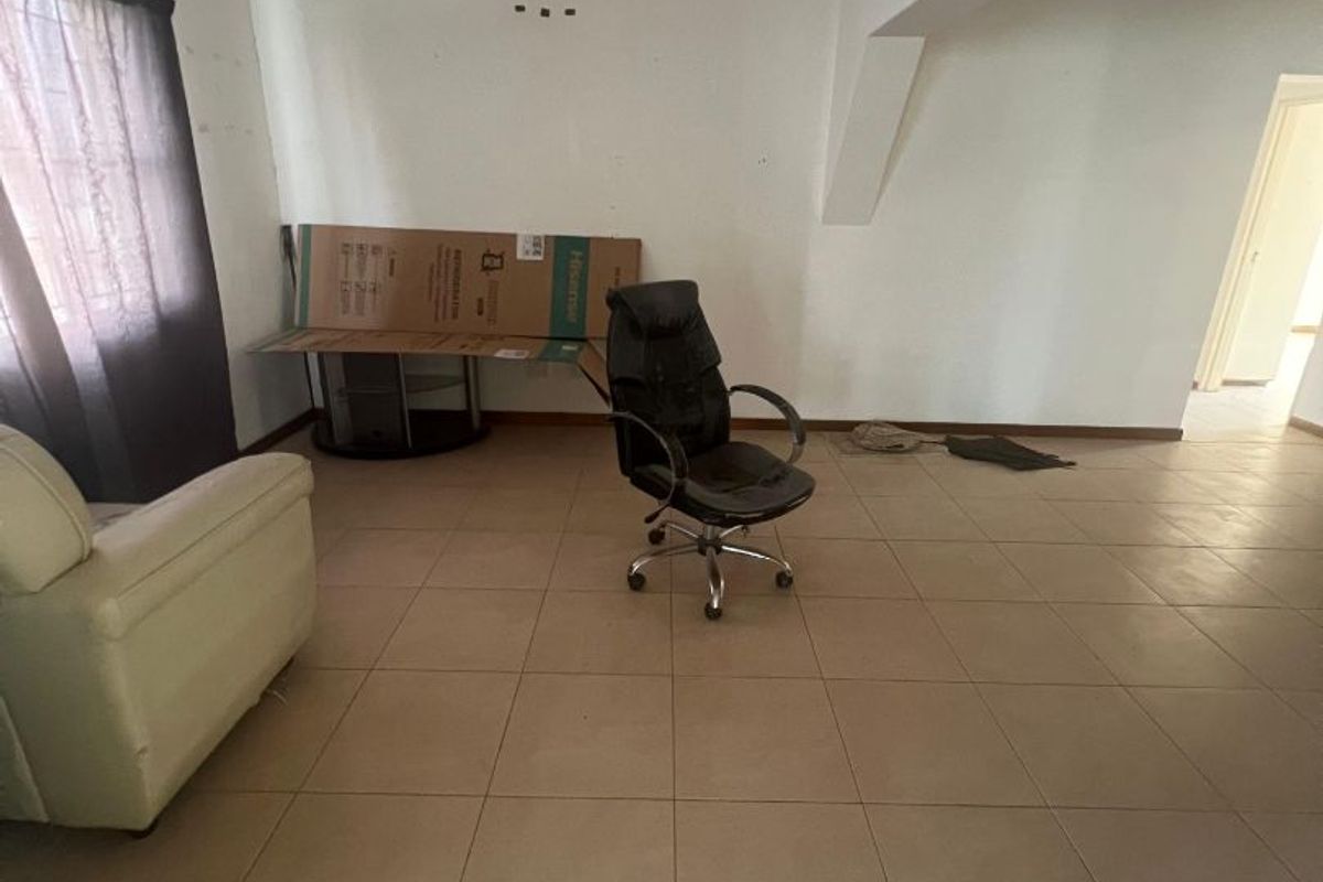 A sparsely furnished living area featuring neutral floor tiles, white walls, and a split-system air conditioning unit.