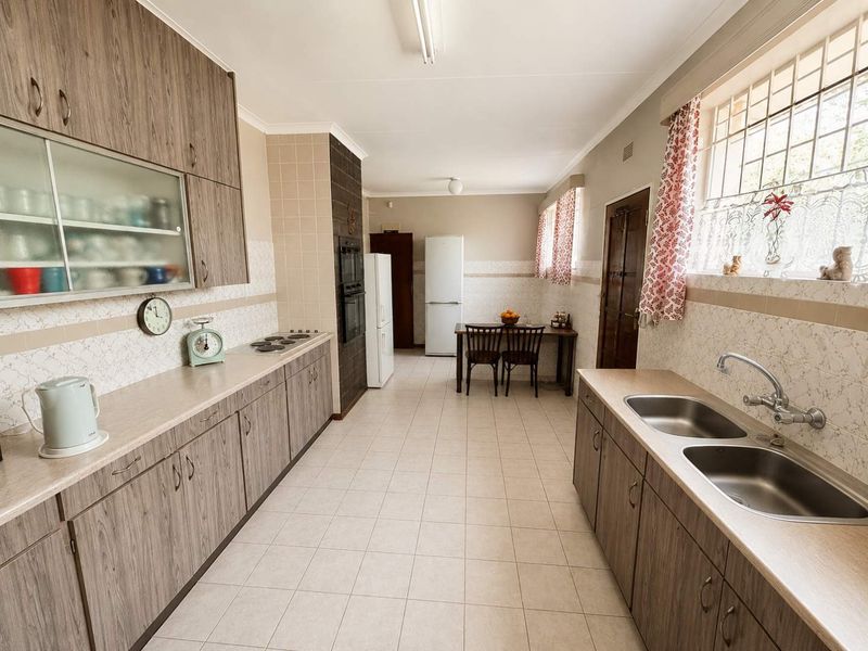 Spacious kitchen featuring wood-look laminate cabinetry, double stainless steel sink, built-in oven, electric hob, and ceramic tiled flooring.