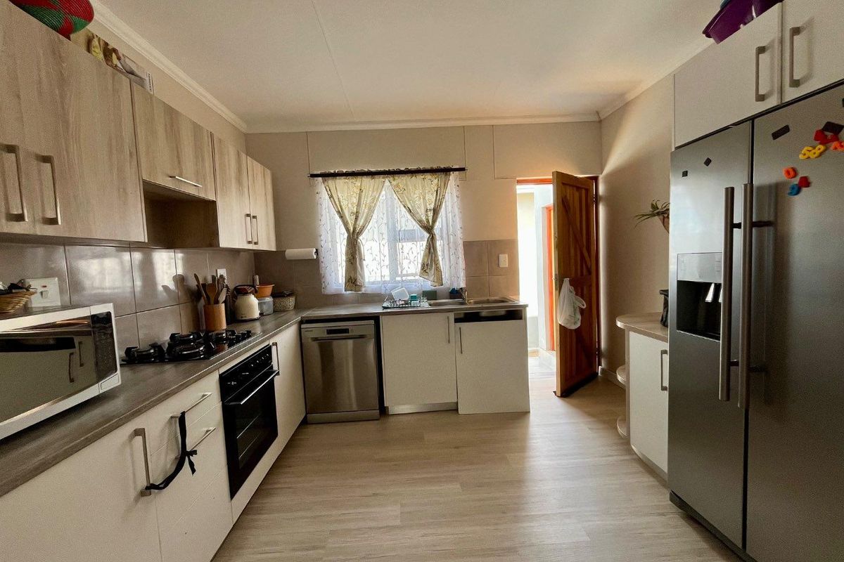 A functional kitchen featuring light wood-look cabinetry, tiled splashbacks, a built-in oven and hob, and direct access to an exterior area.