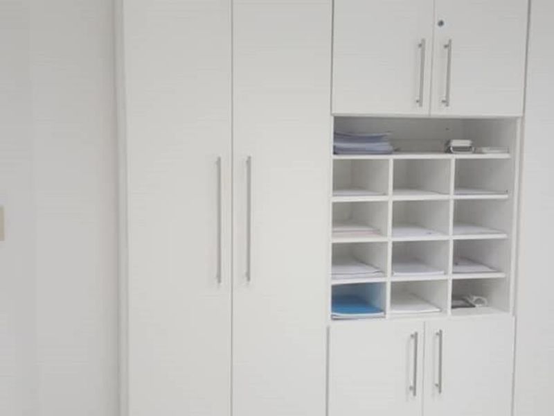 A functional office space featuring white built-in storage cabinetry with integrated pigeonhole shelving and clean tiled flooring.