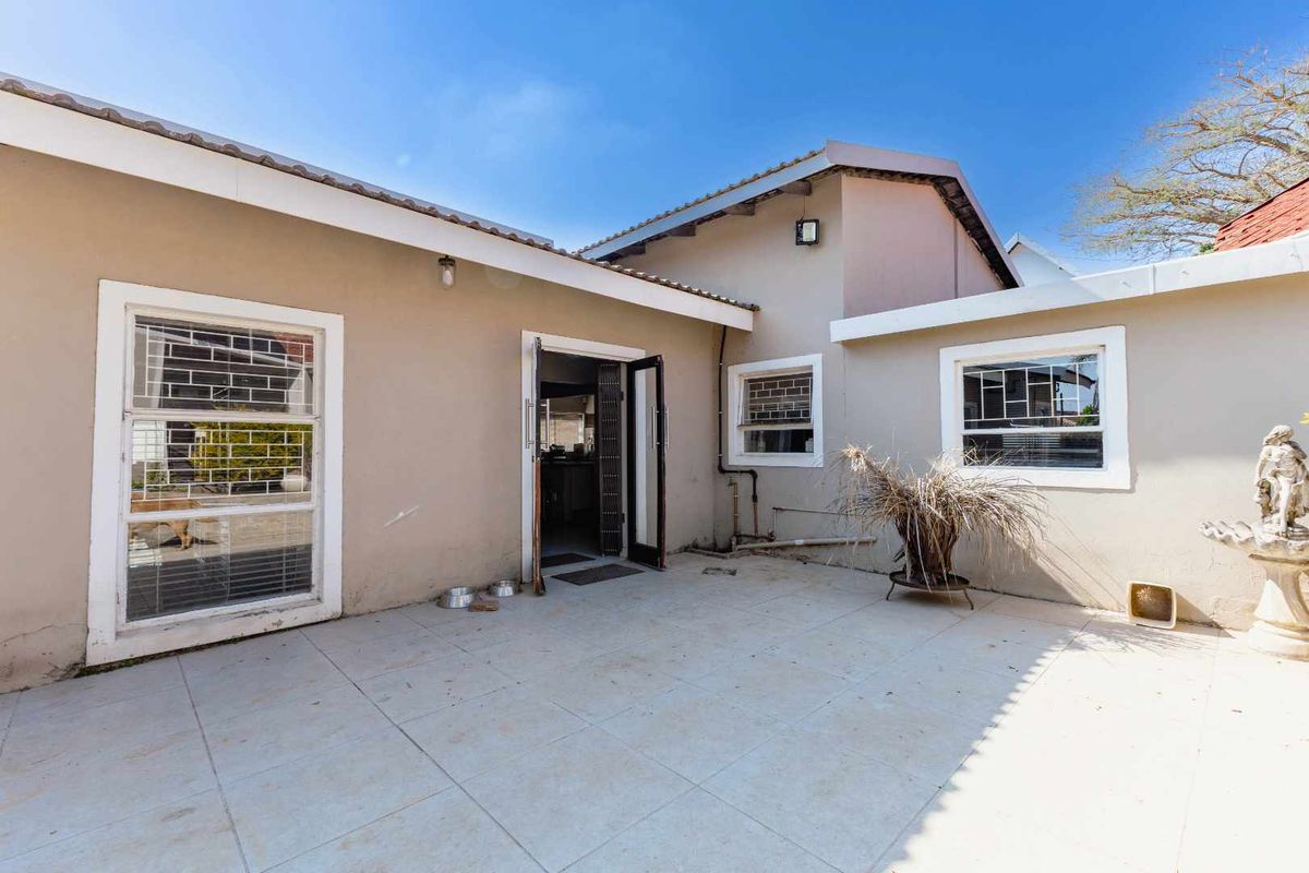 A rear patio area featuring tiled flooring, security-barred windows, and direct access to the interior of the home.