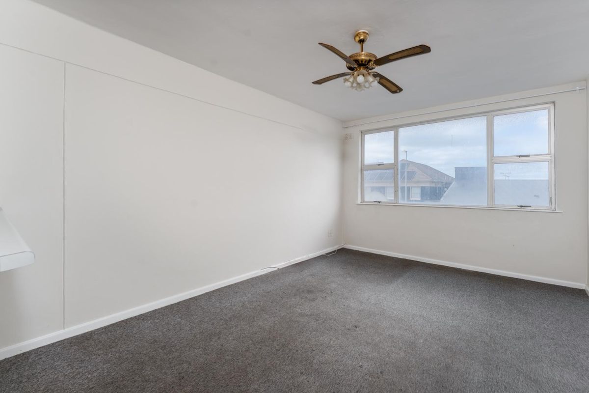 A vacant bedroom featuring neutral walls, grey carpet flooring, and a ceiling fan, offering a blank canvas for personalization.