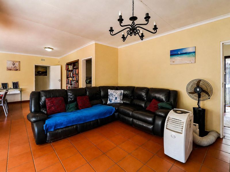A spacious living area featuring terracotta floor tiles, a decorative wrought iron chandelier, and built-in shelving, offering a functional and comfortable layout.