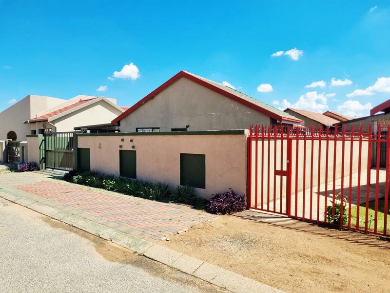 Front exterior view of the property featuring a perimeter wall, red metal security gate, and paved driveway access.