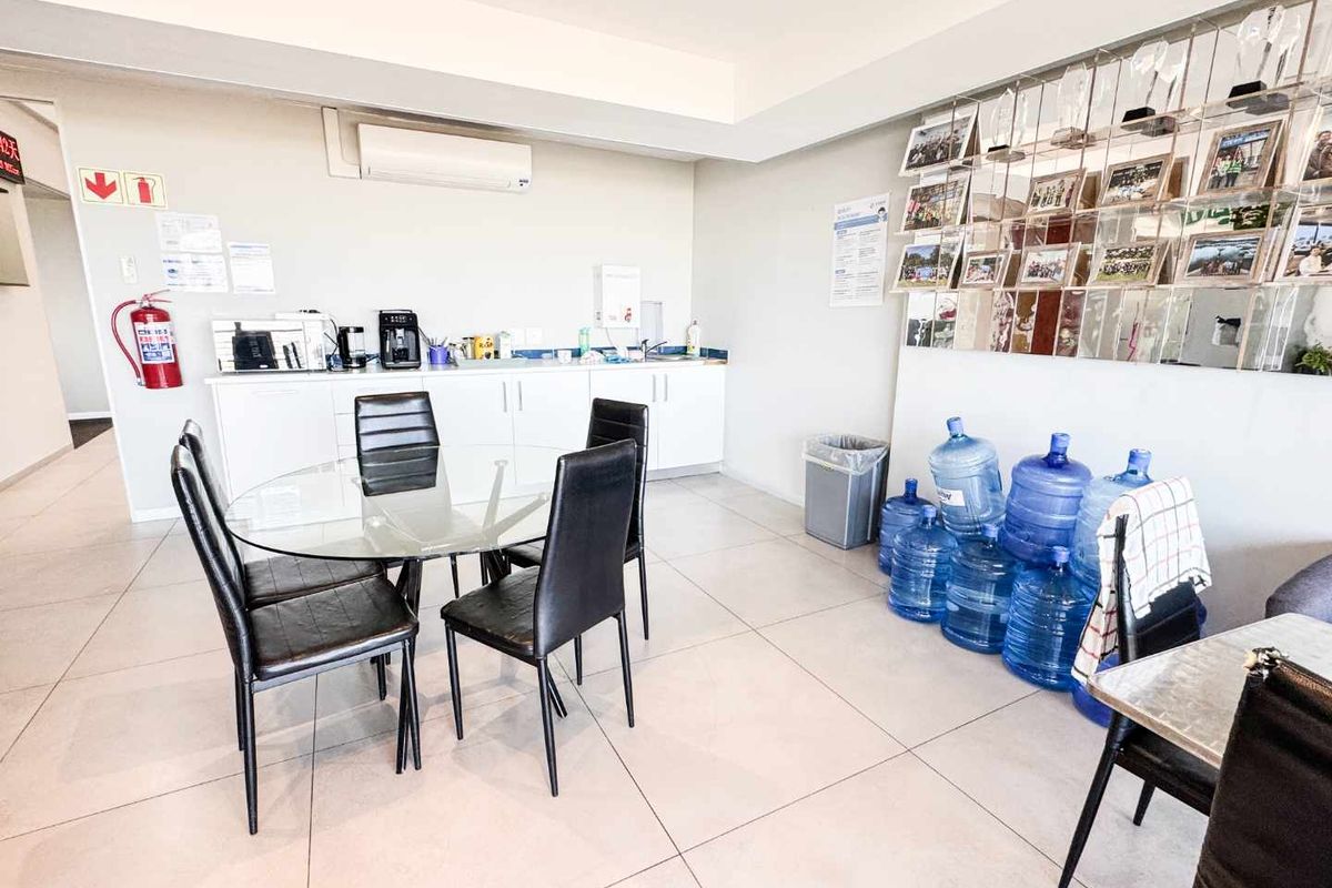 A functional office kitchen area featuring built-in cabinetry, a sink, tiled flooring, and a wall-mounted air conditioning unit.