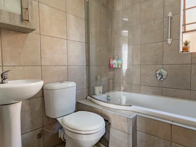 A functional bathroom featuring a pedestal basin, toilet, and a bathtub with a glass shower screen, finished with neutral wall and floor tiles.