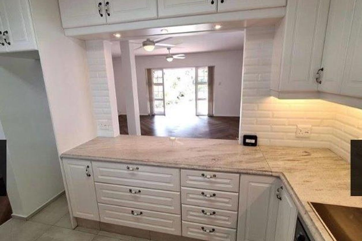 A clean, well-maintained kitchen featuring white cabinetry, stone countertops, and a brick-style backsplash, with a convenient serving hatch overlooking the living area.