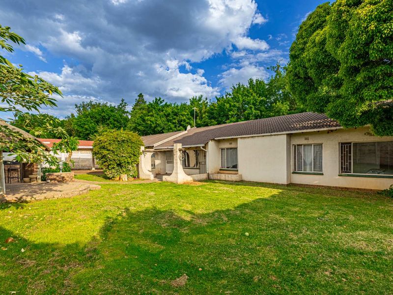 Spacious rear garden featuring a lawn, a covered patio area, and a detached thatched lapa, providing a functional outdoor entertainment space.