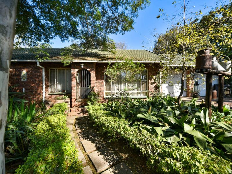 Front view of a single-story brick house featuring a tiled roof, integrated garage, and a mature garden with a paved entrance path.