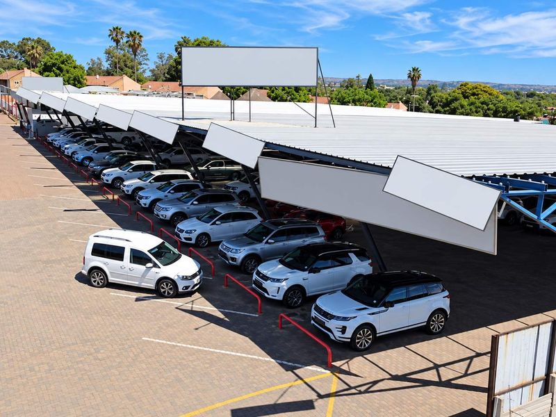 Aerial view of a commercial vehicle dealership featuring a large covered parking canopy with steel structure and paved display area.