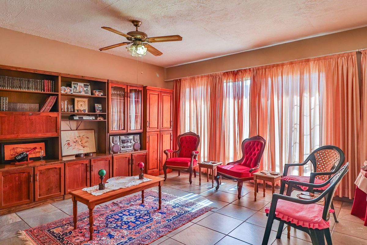 A living room featuring built-in wooden cabinetry, tiled flooring, and a ceiling fan, with large windows covered by curtains.