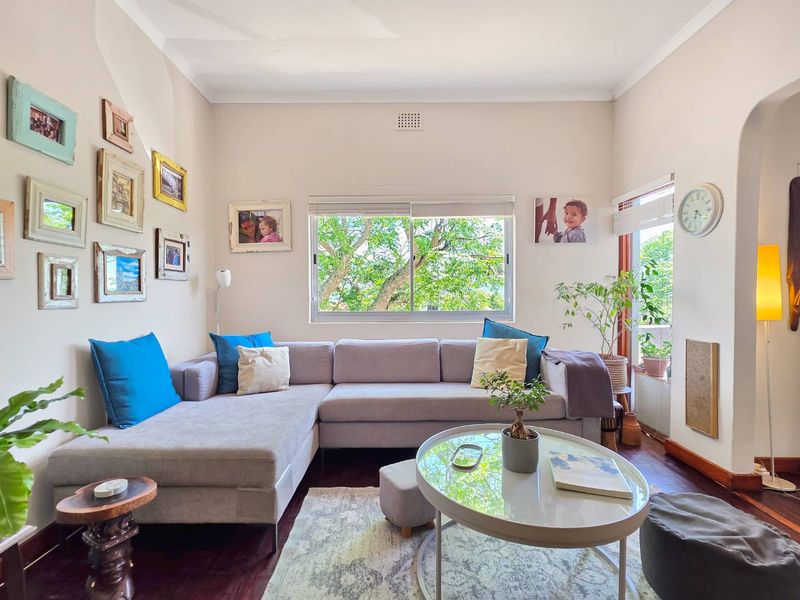 A bright and inviting living room featuring polished hardwood flooring, an arched entryway, and a large window providing natural light and garden views.