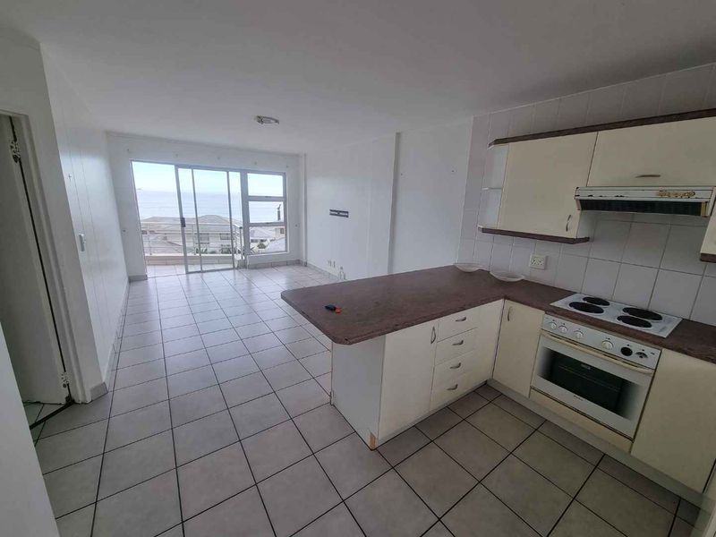Open-plan kitchen and living area featuring tiled floors, built-in cabinetry, and sliding glass doors leading to a balcony with ocean views.