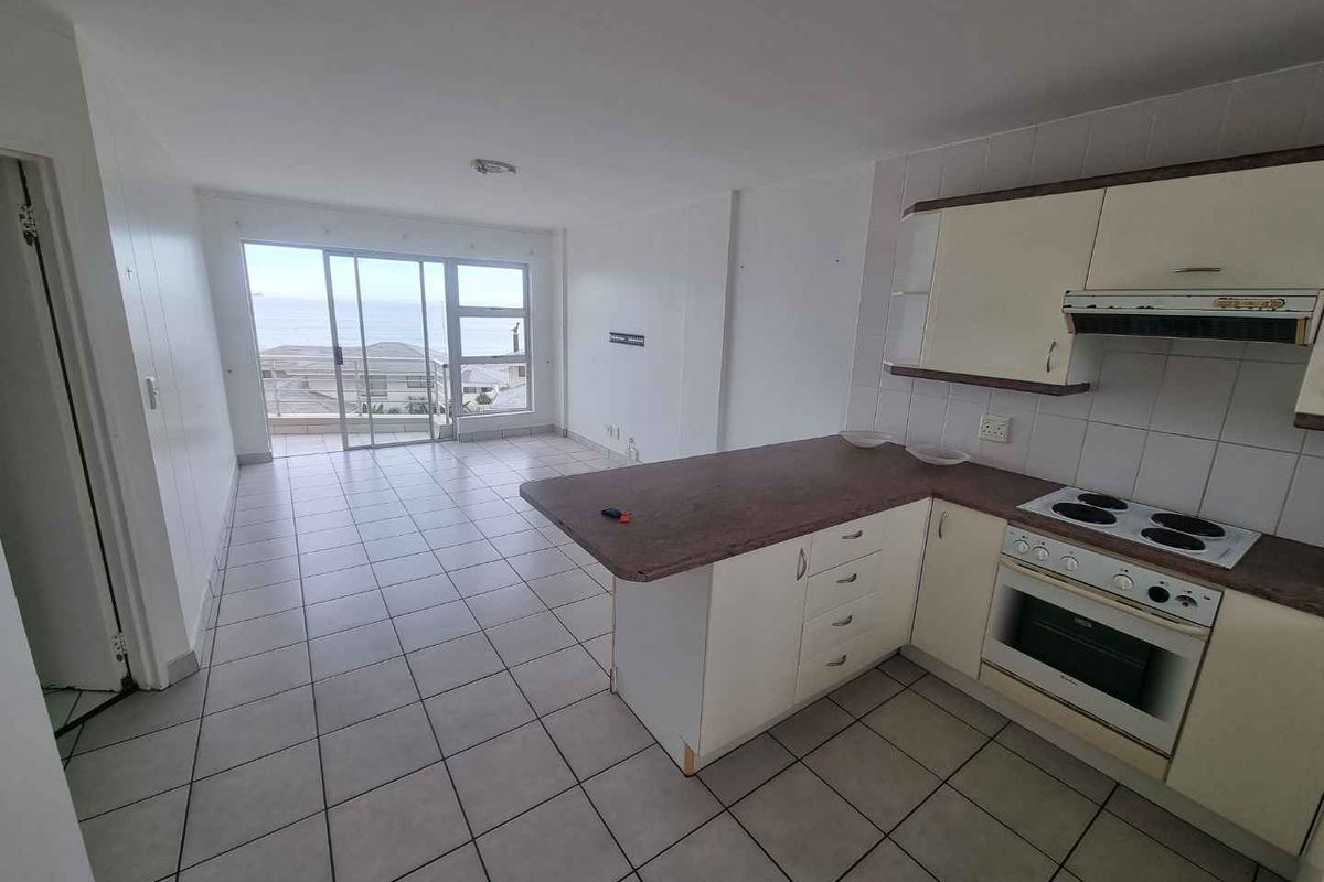 Open-plan kitchen and living area featuring tiled floors, built-in cabinetry, and sliding glass doors leading to a balcony with ocean views.