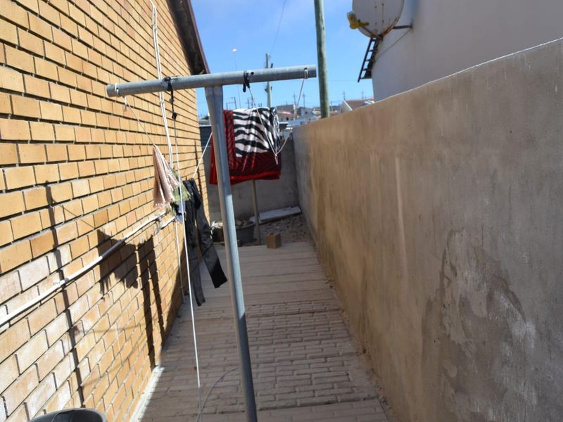 A narrow side passage featuring a brick wall, a concrete boundary wall, and paved flooring, currently used as a utility area.