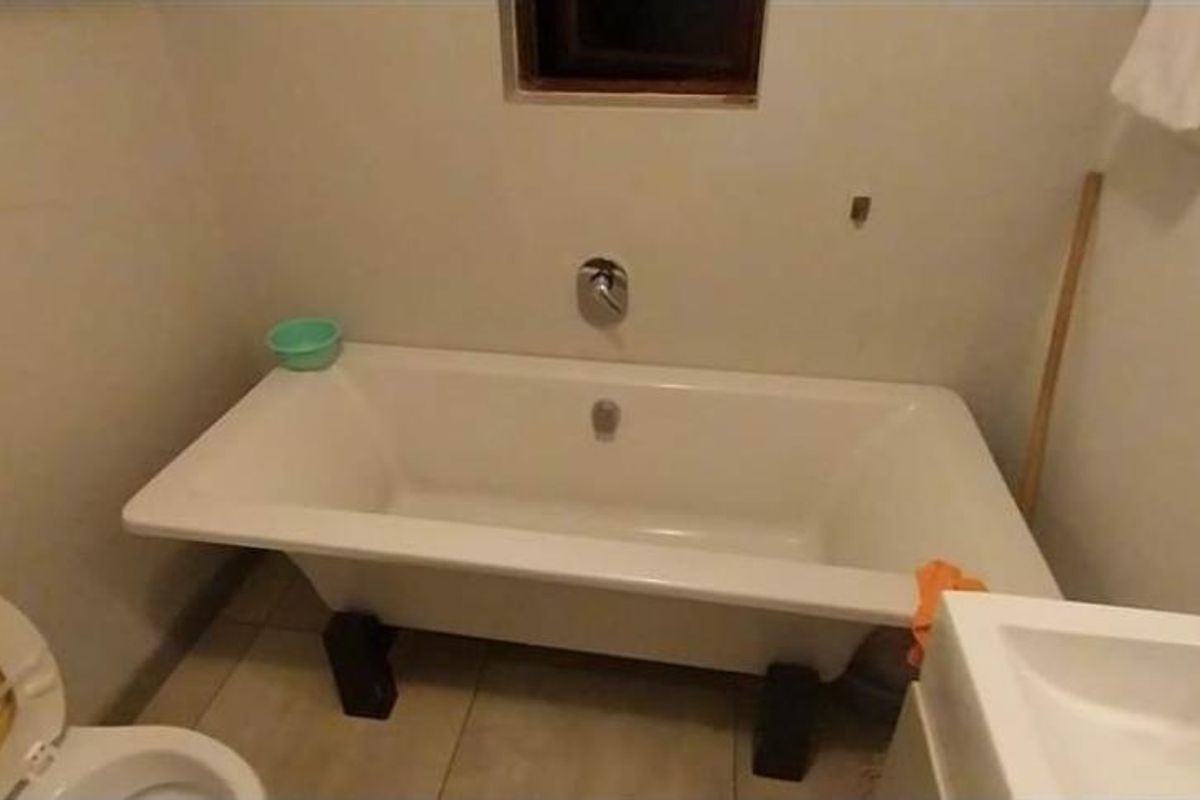 A functional bathroom featuring a freestanding bathtub, a standard toilet, and a wall-mounted basin, requiring some cosmetic updates and finishing touches.