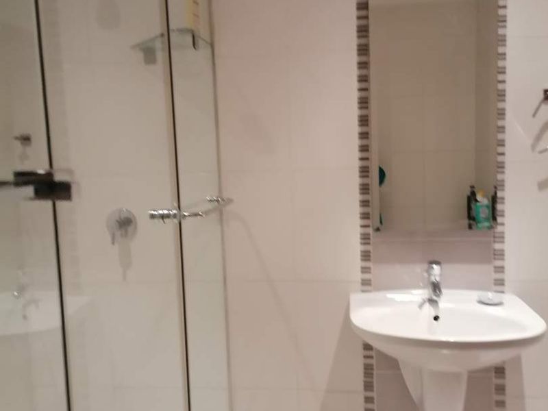 A clean, modern bathroom featuring a glass-enclosed shower, wall-mounted basin, and neutral wall tiling.