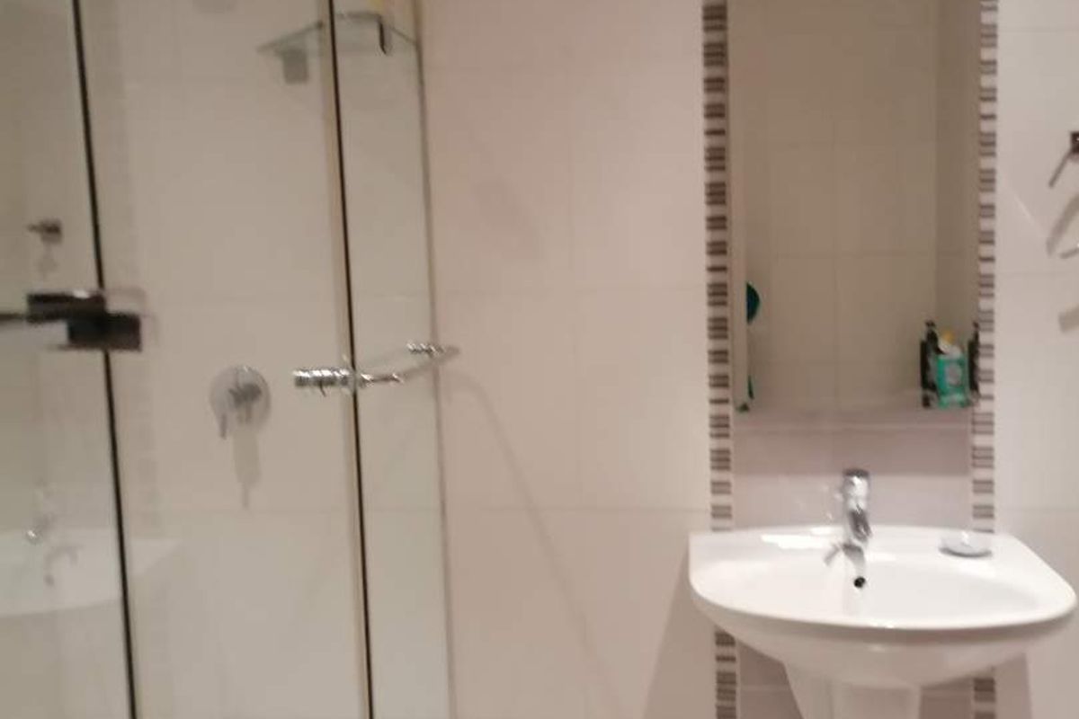 A clean, modern bathroom featuring a glass-enclosed shower, wall-mounted basin, and neutral wall tiling.
