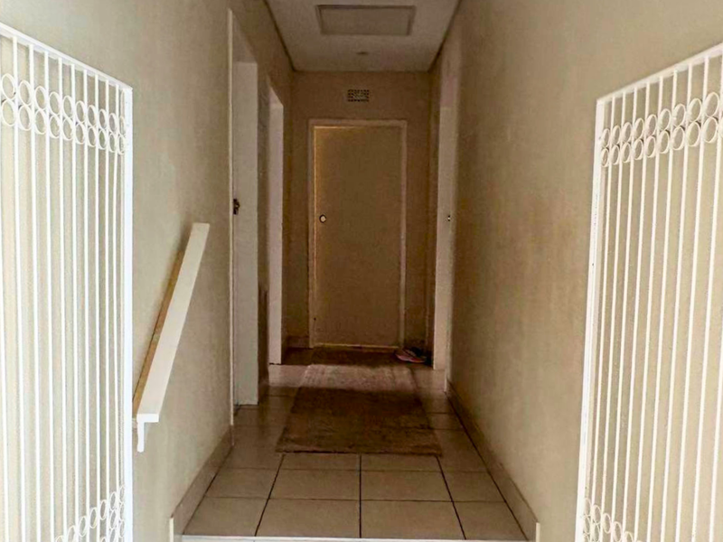 A narrow interior hallway featuring tiled flooring, a handrail, and white security gates at the entrance.
