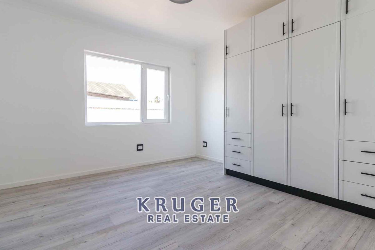 A bright, empty bedroom featuring modern light-toned laminate flooring and extensive floor-to-ceiling built-in cabinetry with white finishes.