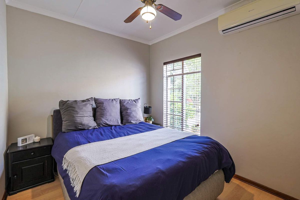 A well-lit bedroom featuring laminate flooring, a ceiling fan, and a wall-mounted air conditioning unit.