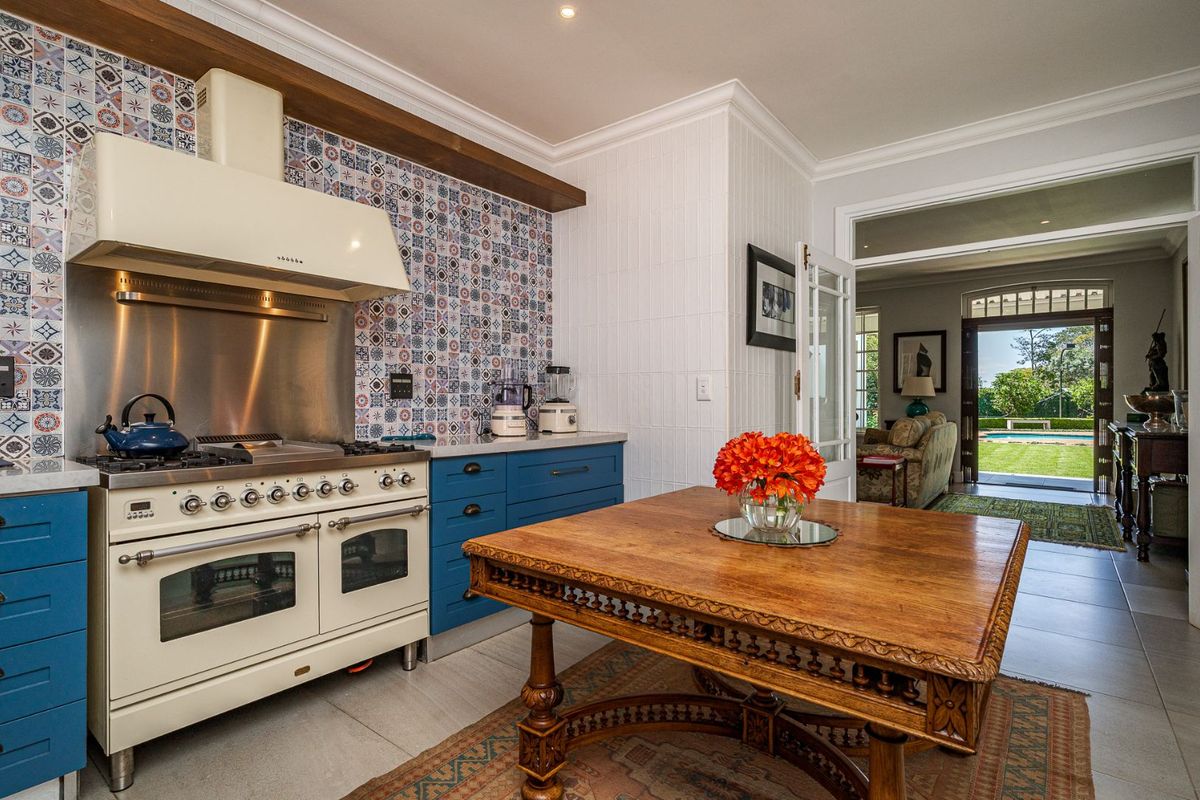 A well-appointed kitchen featuring a classic gas range cooker, decorative patterned tile backsplash, and blue cabinetry, with direct access to an outdoor patio area.