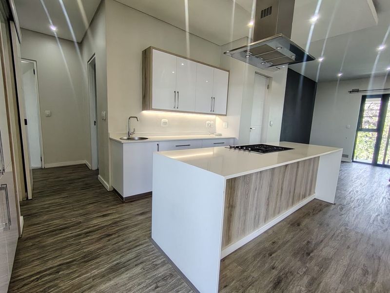 Modern kitchen featuring a central island with a gas cooktop, sleek white cabinetry, stone countertops, and high-quality laminate flooring in an open-plan layout.