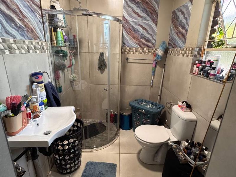 Compact bathroom featuring a curved glass shower enclosure, wall-mounted basin, toilet, and decorative tiled accents with a leaded glass window.
