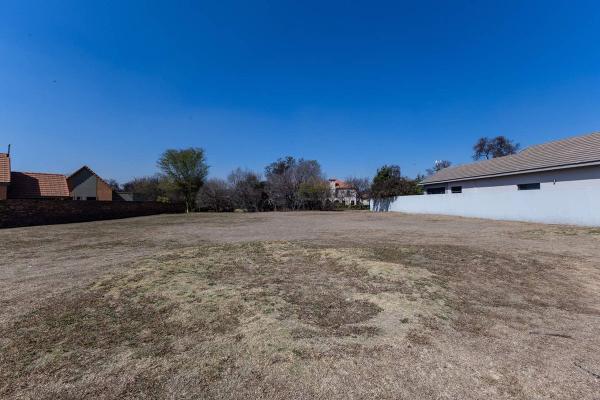 A vacant residential plot featuring dry grass, enclosed by perimeter walls and boundary fencing, offering a clear space for future development.