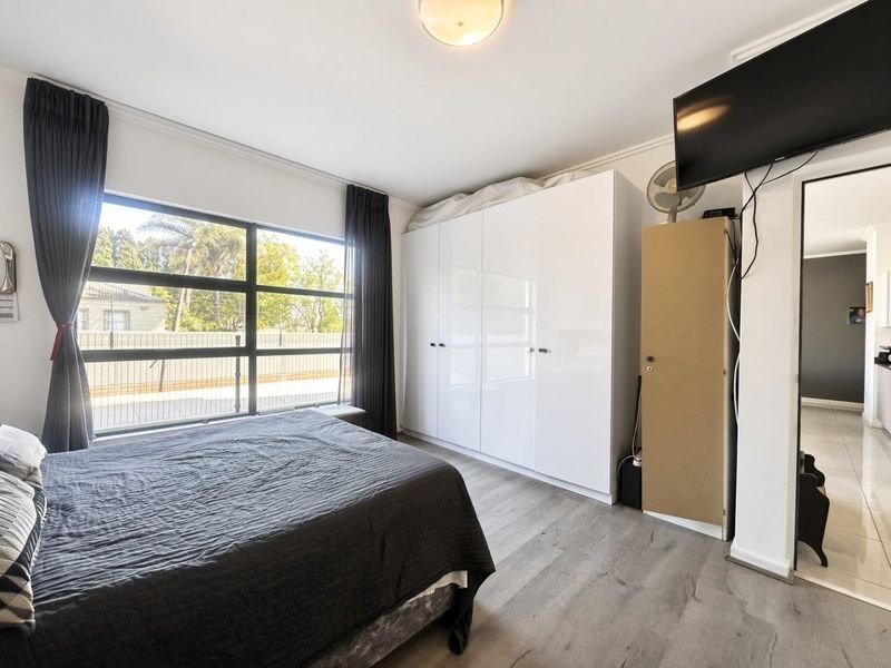 A well-lit bedroom featuring modern laminate flooring, a large window providing natural light, and ample built-in cupboard storage space.