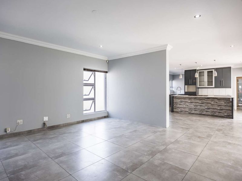 Spacious open-plan living area featuring large format floor tiles, recessed lighting, and a modern kitchen with a stone-clad island and dark cabinetry.